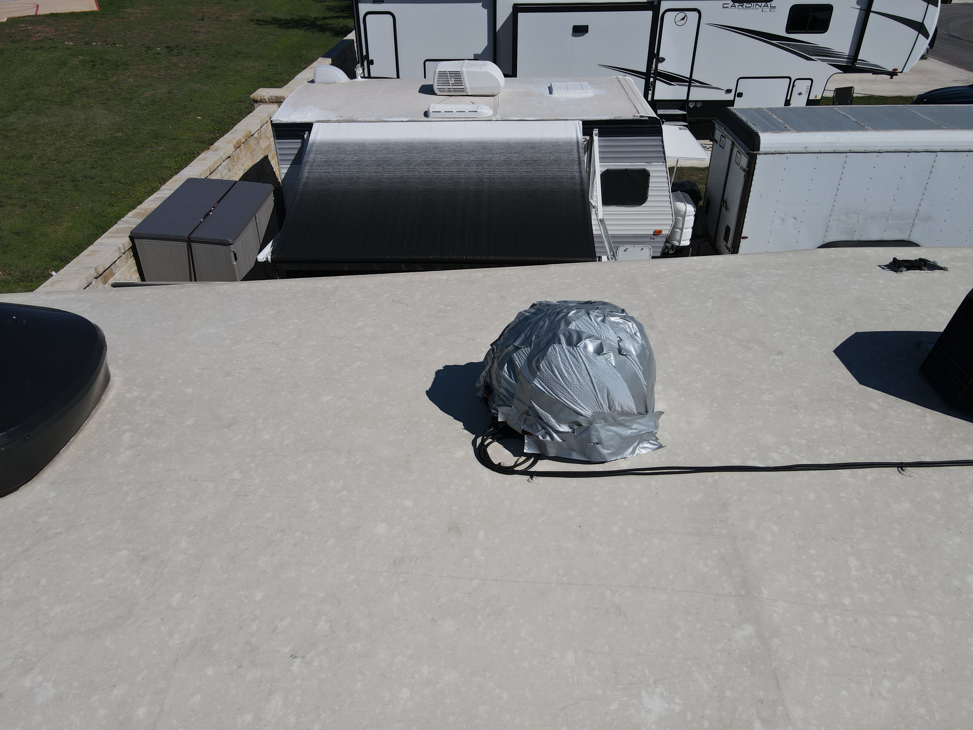 RV roof showing a satellite dome entirely wrapped in silver duct tape to cover hail damage — chalky aged membrane, coaxial cable running across the surface — Boss Bull Mobile RV Services