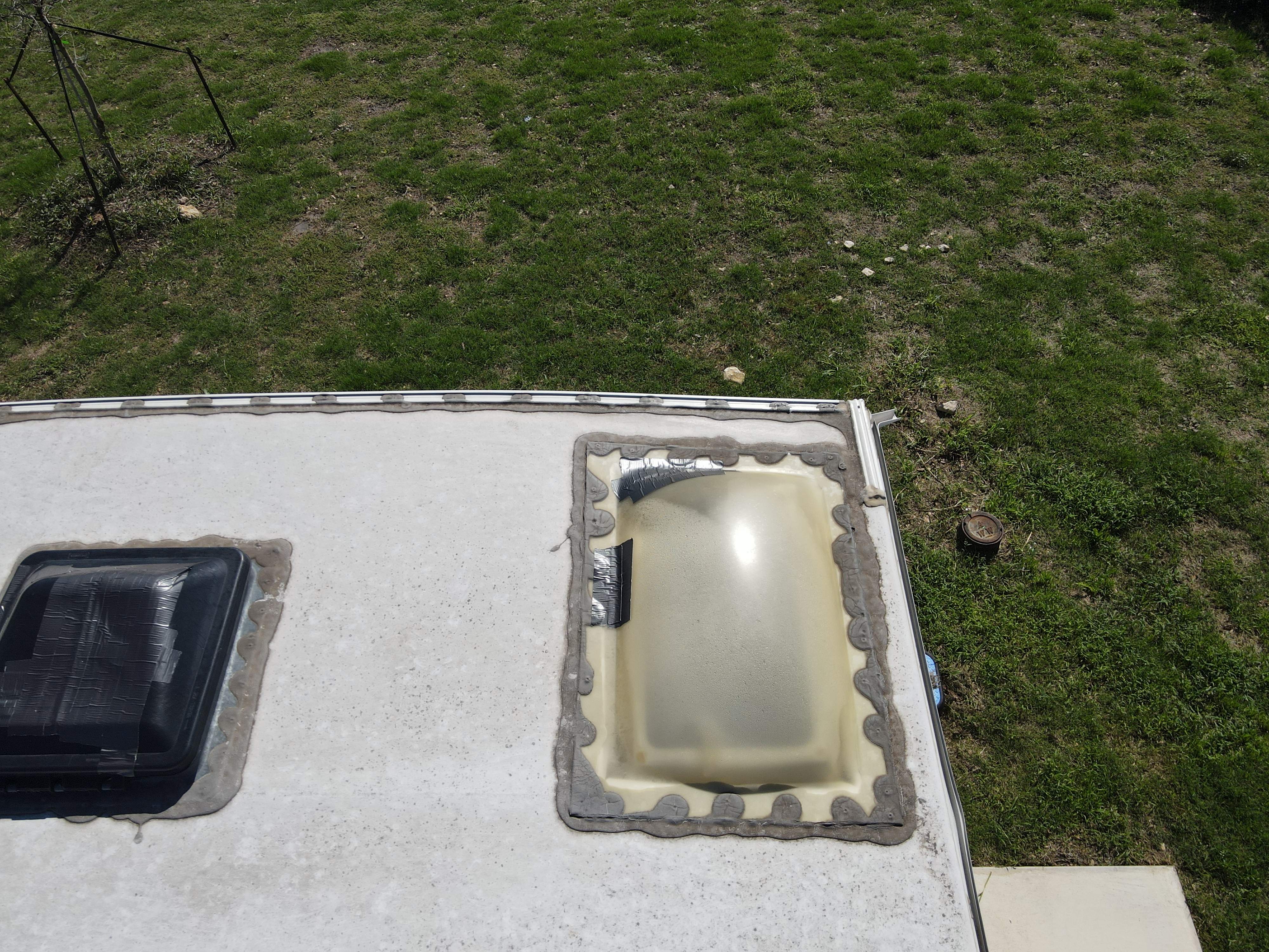 Close overhead view of an RV roof corner showing a UV-crazed yellowed skylight dome with duct tape patch and failed DIY sealant — hail and storm damage documentation — Boss Bull Mobile RV Services
