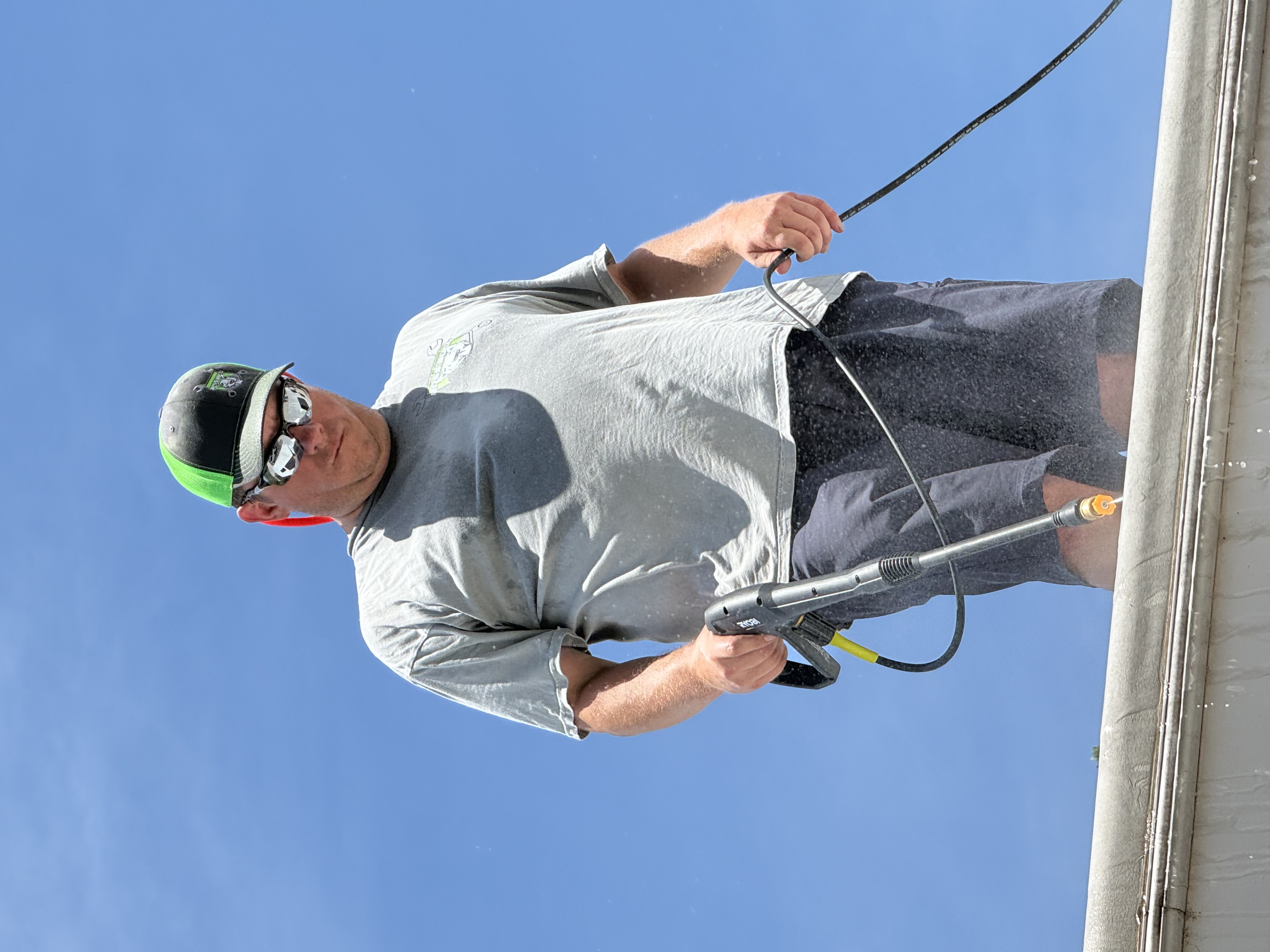 Boss Bull technician standing on an RV roof edge pressure washing the membrane surface during roof cleaning and surface preparation before Crazy Seal coating application — blue sky background — Boss Bull Mobile RV Services