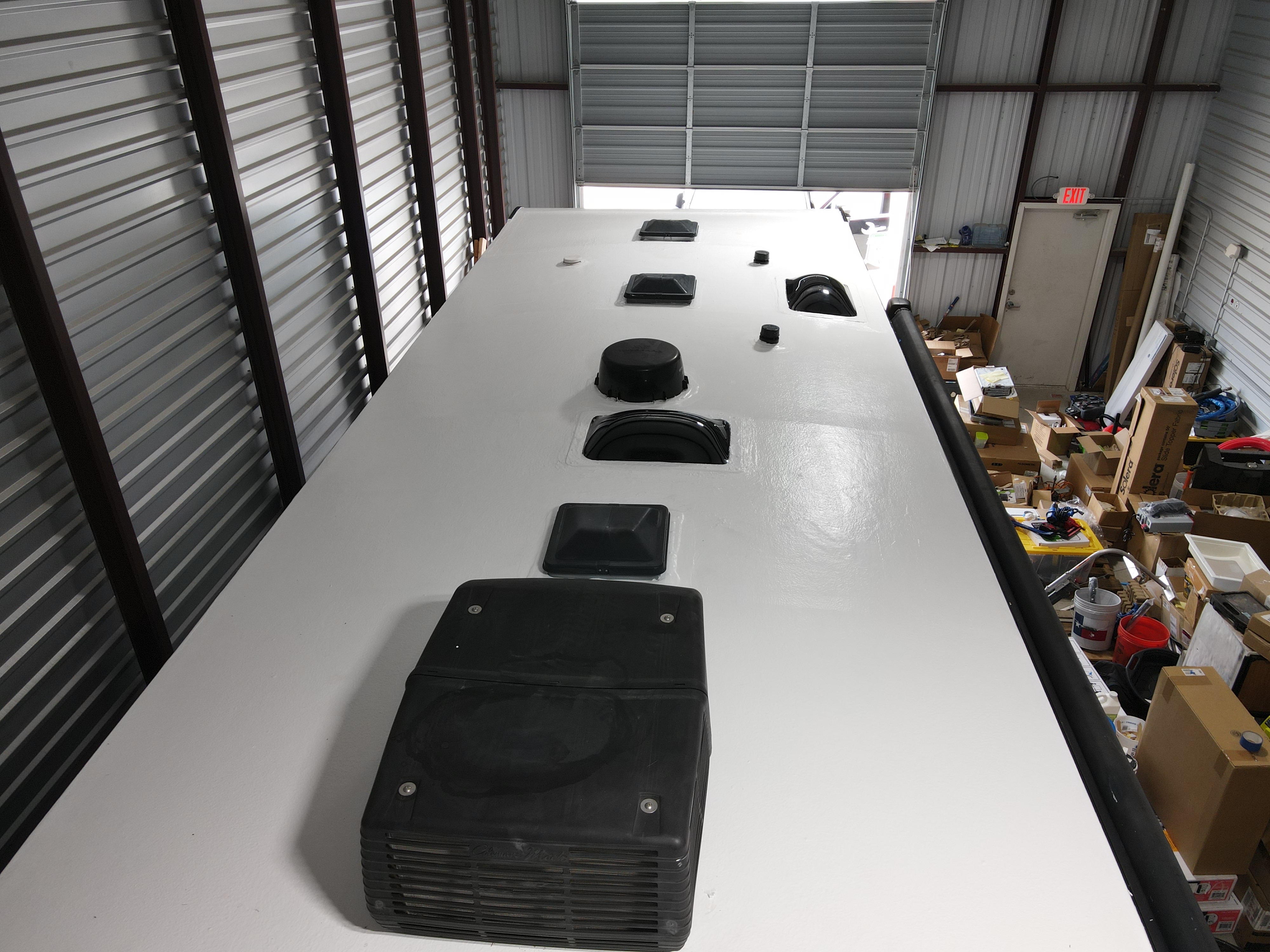 Shop interior overhead view of a completed Crazy Seal RV roof system installation on a Crossroads Cameo fifth-wheel — bright white elastomeric coat fully applied, all six penetrations reinstalled and sealed — Boss Bull Mobile RV Services